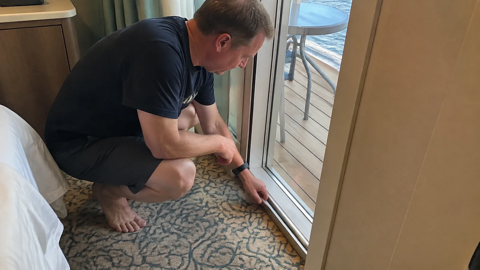 Passenger examining the sliding-door track at a cabin balcony threshold.