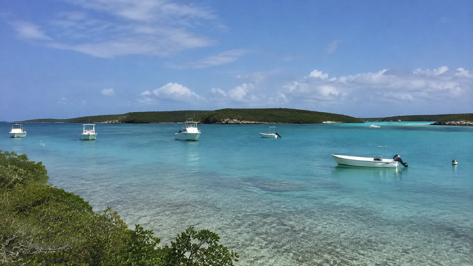 Small boats anchored in clear blue water beside low green islands.
