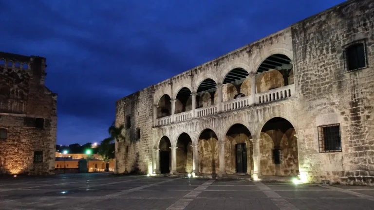 Illuminated historic stone building with two levels of arches at dusk.