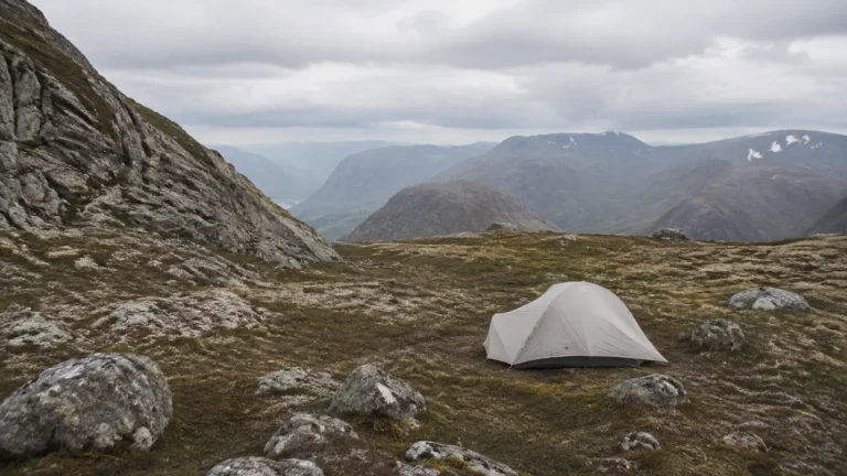 Small tent pitched on rocky alpine ground overlooking distant mountains.