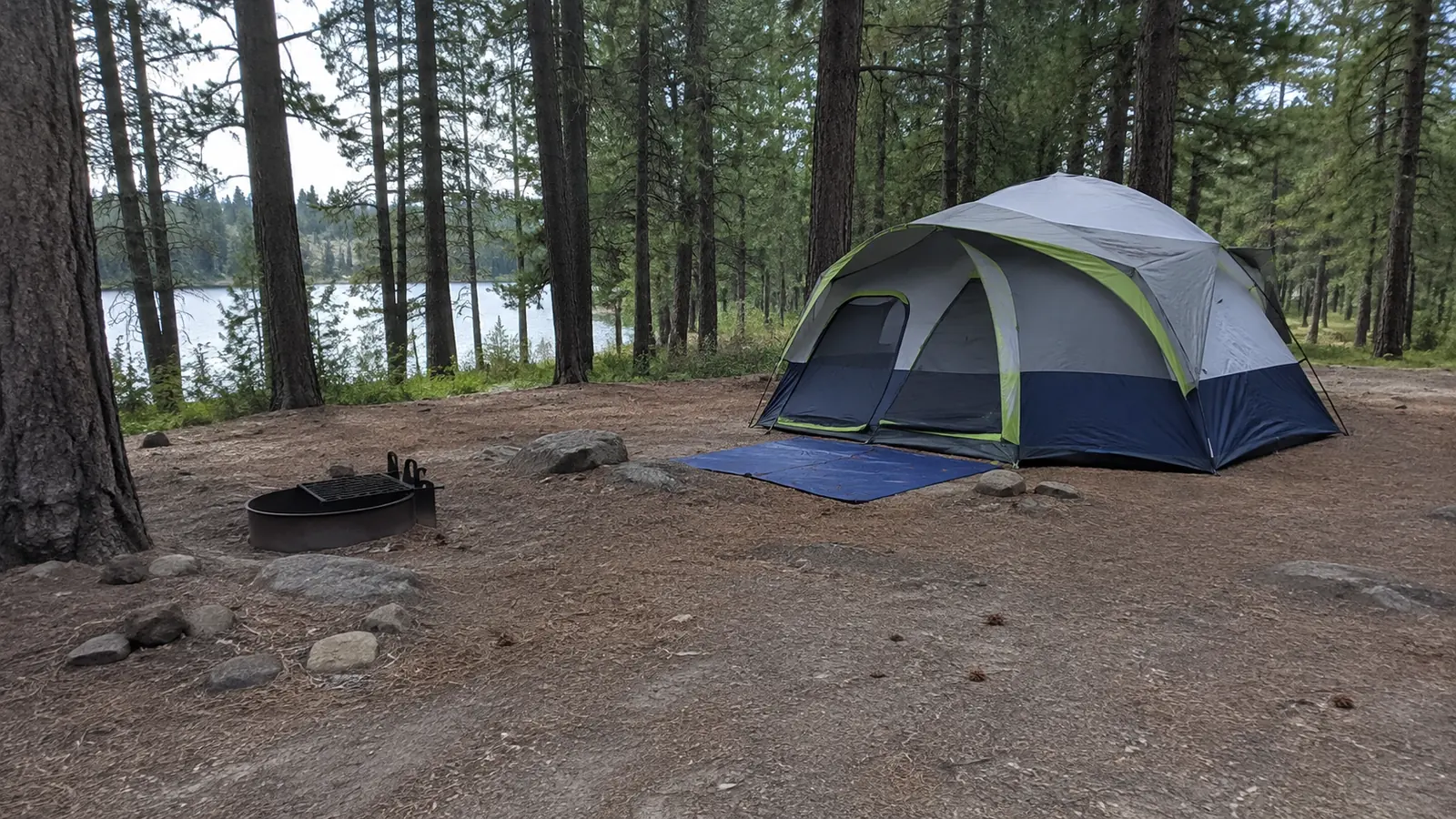 Large tent and fire ring at a forested lakeside campsite.
