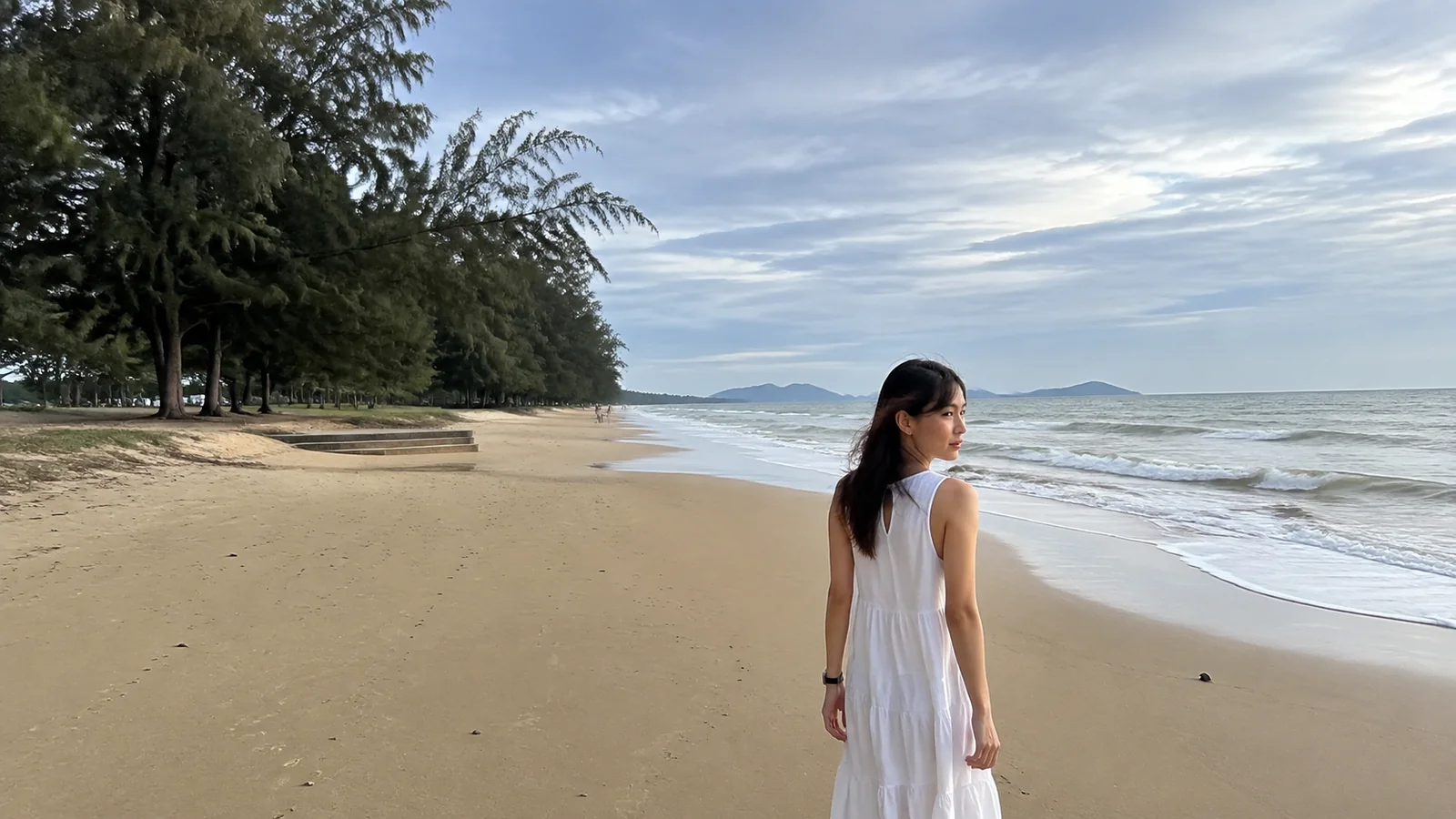 Woman walking along a quiet sandy beach beside gentle waves.