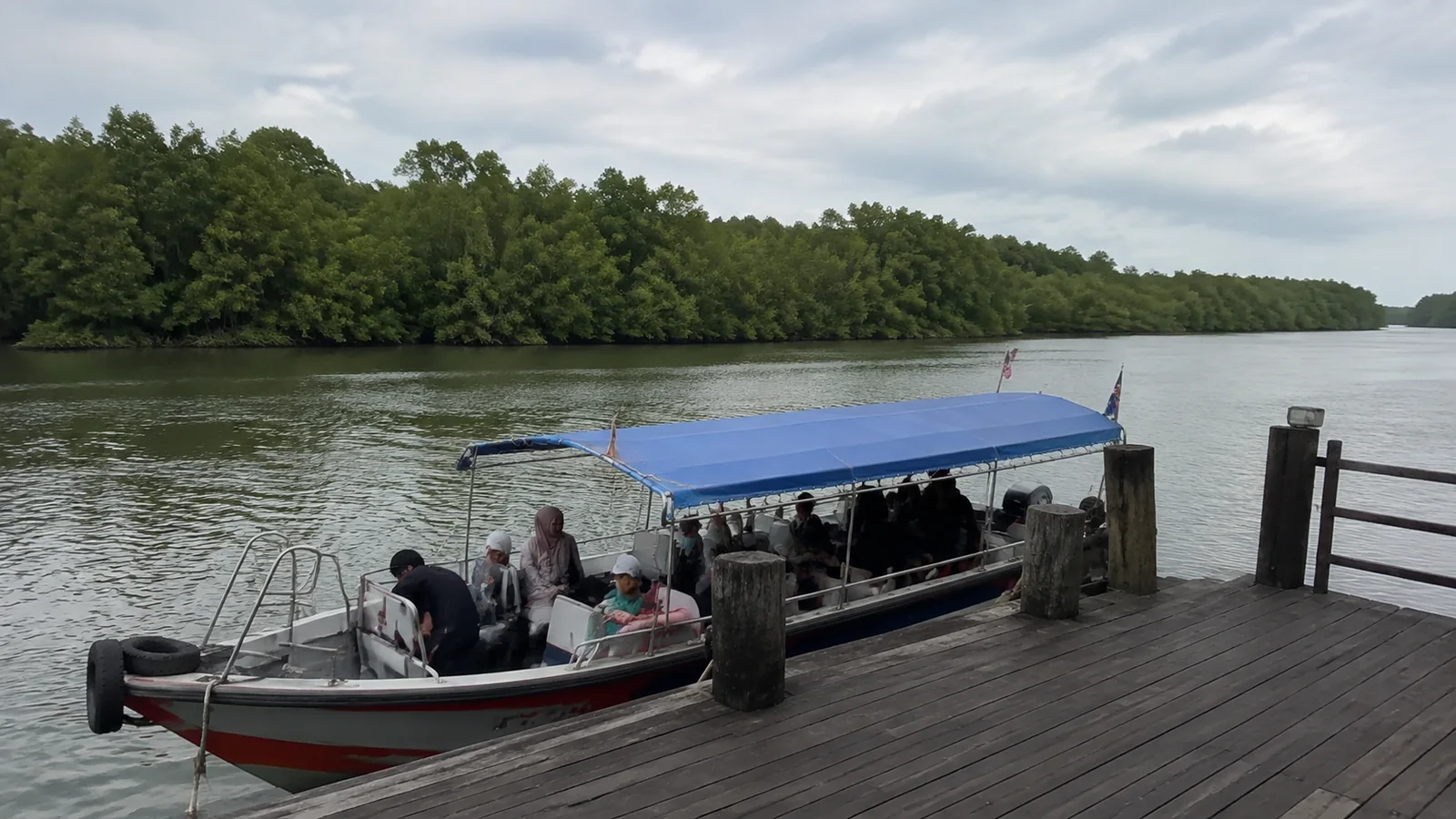 Passengers boarding a covered boat beside a mangrove-lined river.
