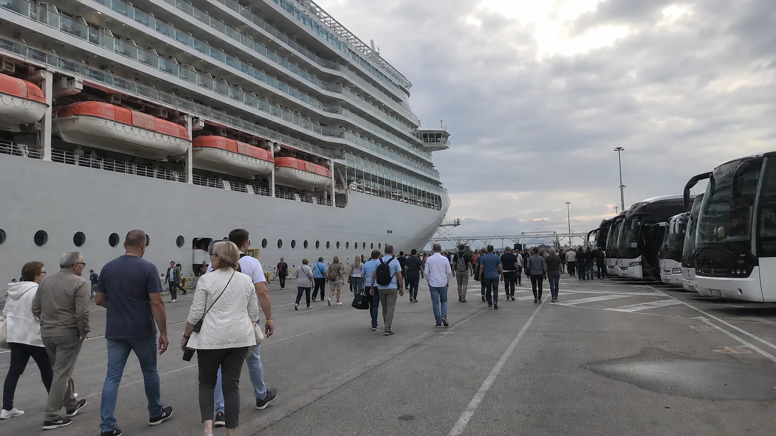 Cruise passengers walking between a docked ship and waiting coaches.