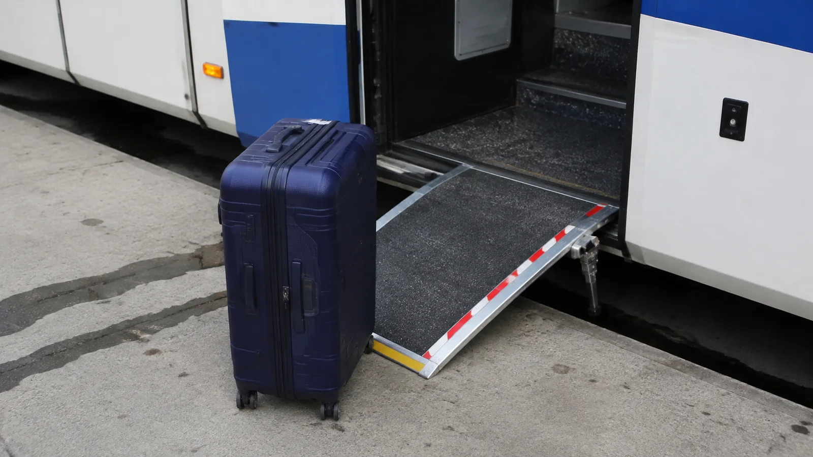 Rolling suitcase beside a lowered bus boarding ramp.
