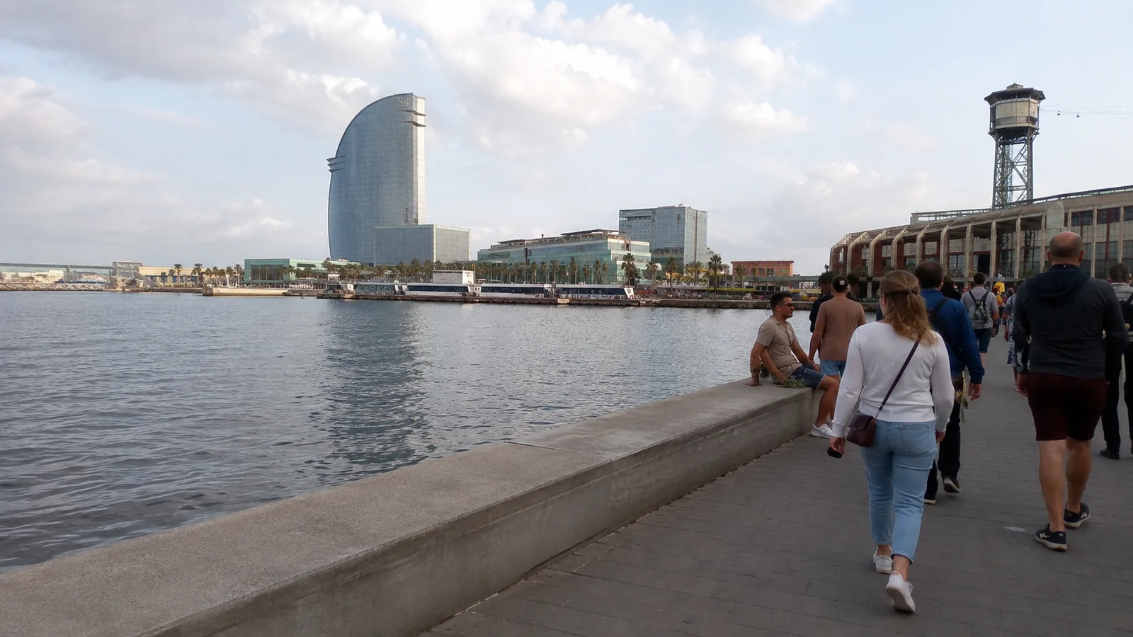People strolling along Barcelona's waterfront with the sail-shaped hotel across the water.