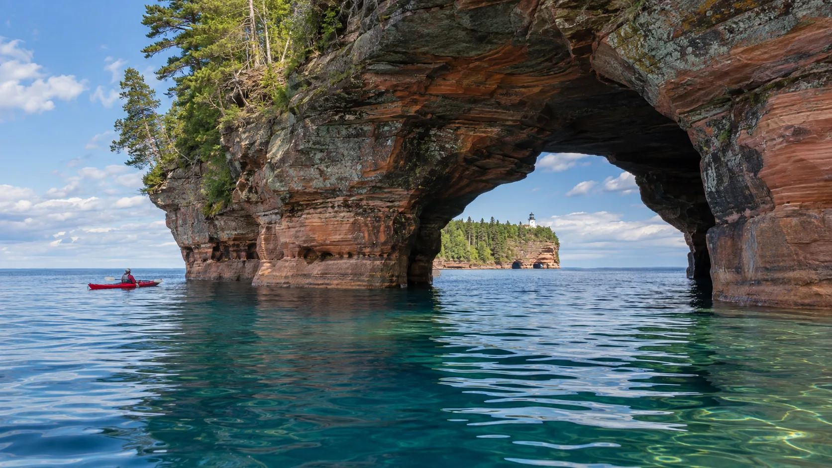 Red sandstone sea cave, kayak and distant lighthouse in the Apostle Islands near Bayfield, Wisconsin