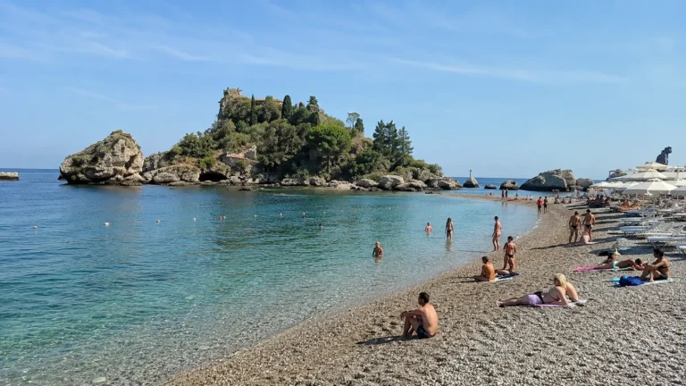 Pebble beach with clear blue water and a small rocky island offshore