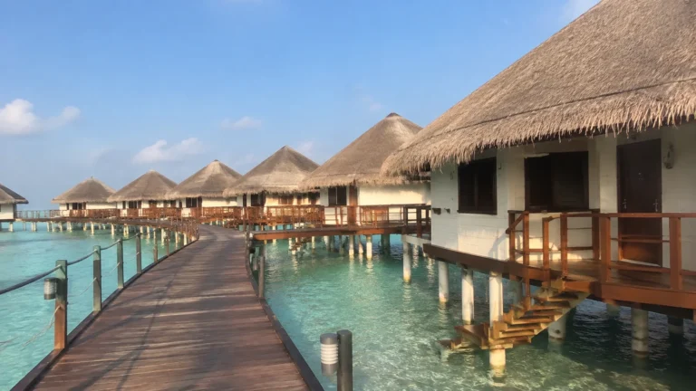 Wooden boardwalk winding between thatched overwater bungalows above a clear lagoon.
