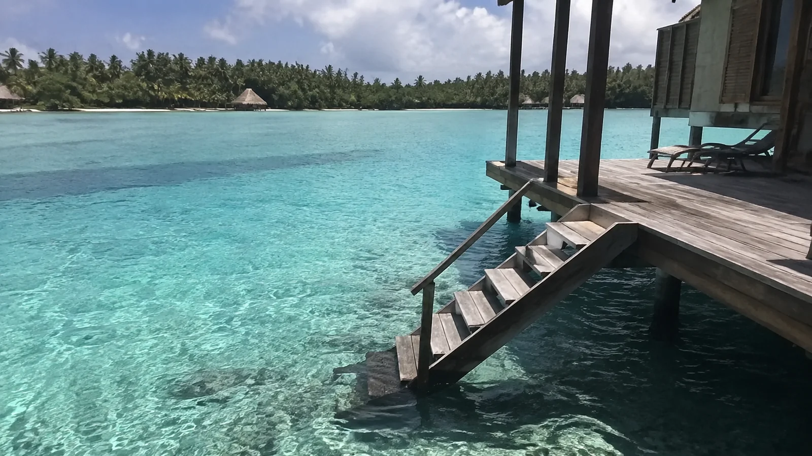 Wooden steps leading from a private bungalow deck into turquoise water.