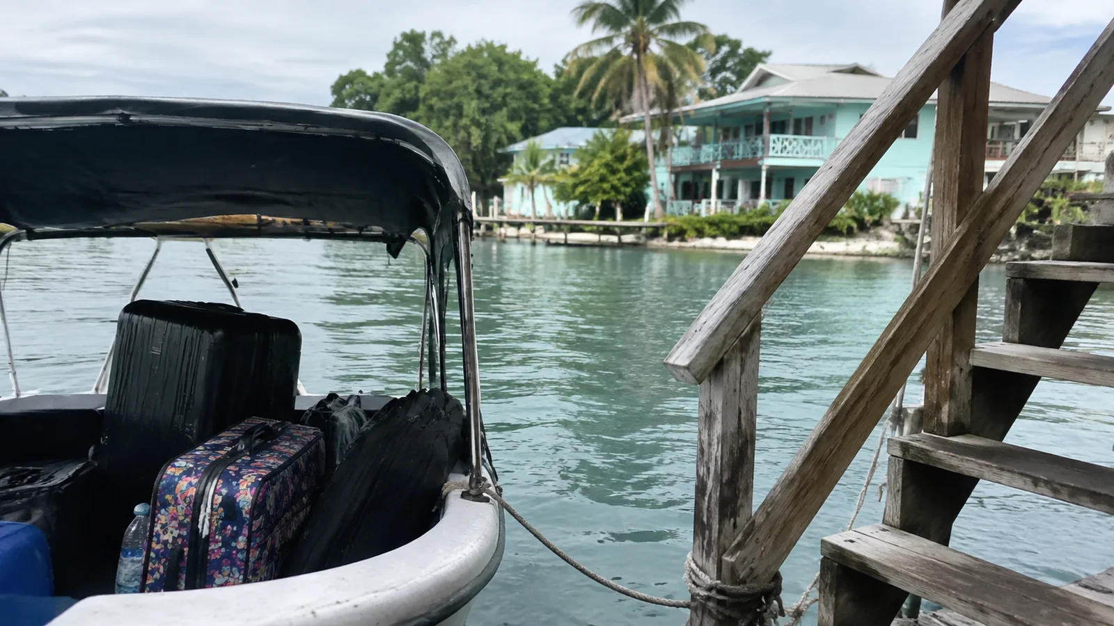 Luggage in a small covered boat beside wooden dock steps.
