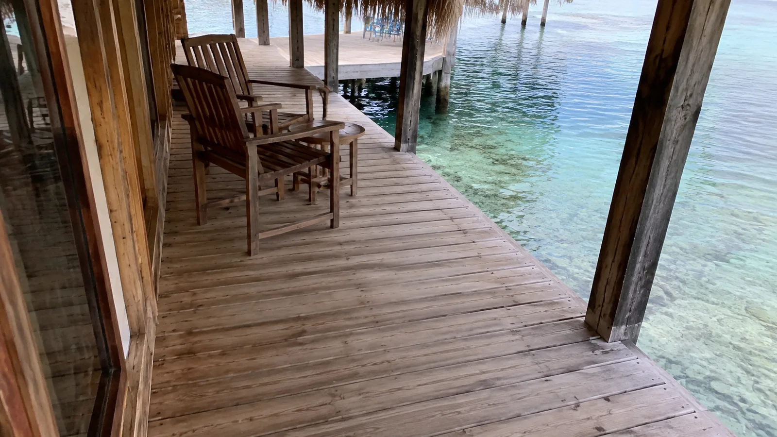 Wooden chairs on a shaded bungalow deck above clear water.
