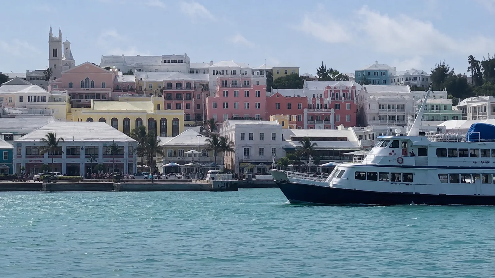 Ferry crossing in front of pastel-colored harbor buildings.