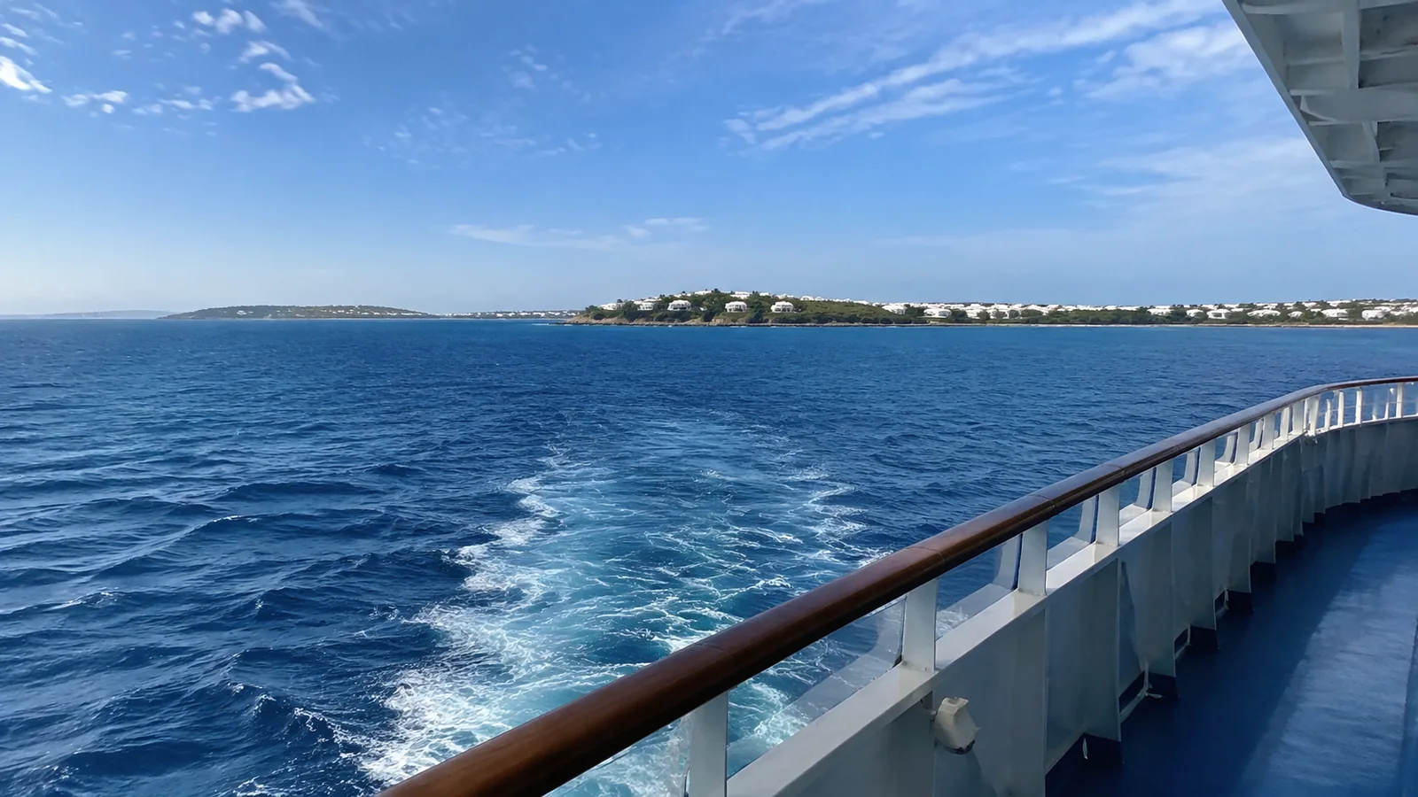 Ship's wake curving through deep blue water near a low coastline.