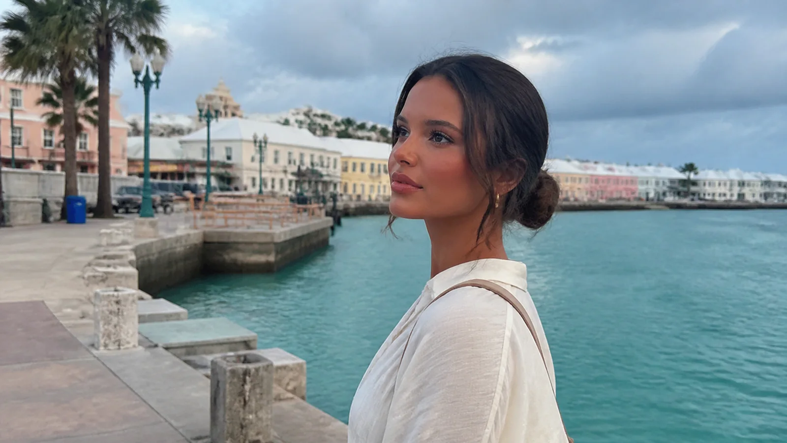Woman standing beside a harbor lined with pastel buildings.