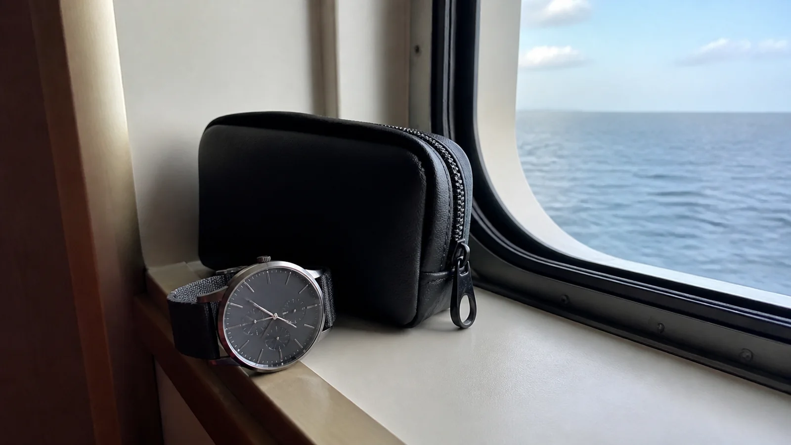 Watch and zippered pouch on a ship windowsill overlooking the sea.