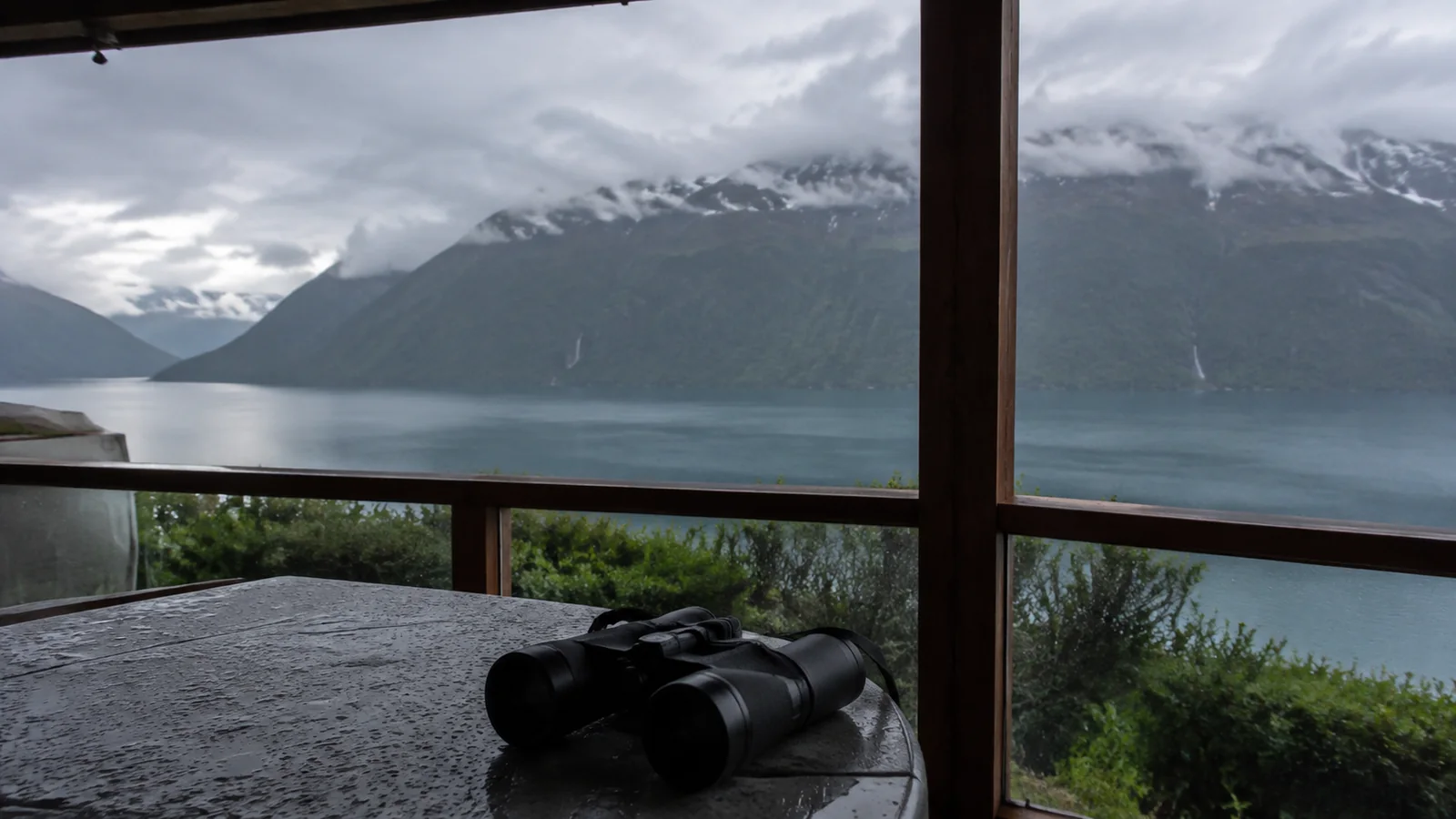 Binoculars on a table beneath windows overlooking misty mountains and water.