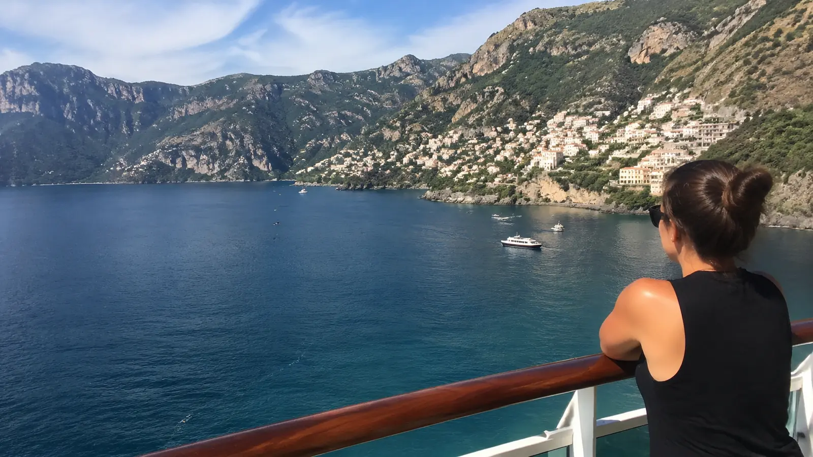 Woman standing at a cruise ship railing overlooking a coastal town and mountains