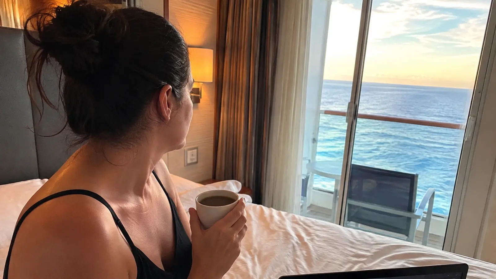 Woman holding a coffee cup inside a cruise cabin while looking out at the ocean