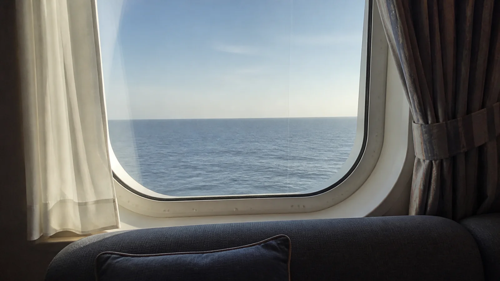 Ocean horizon is visible through a stateroom window above a sofa.