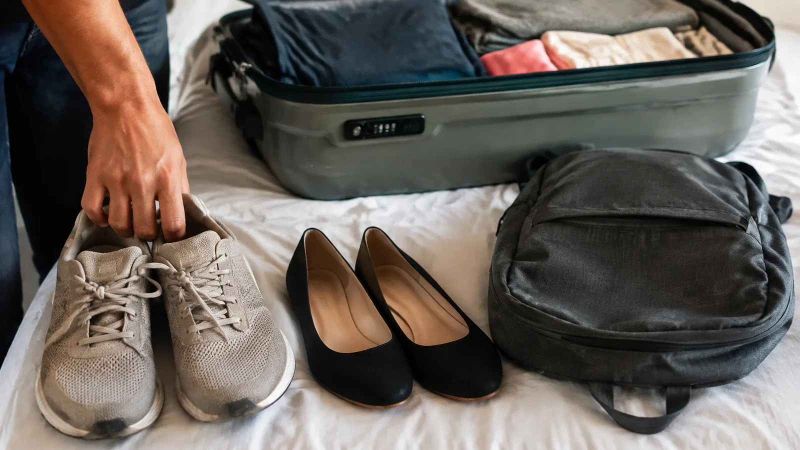Walking shoes, dress shoes and a backpack beside an open suitcase.