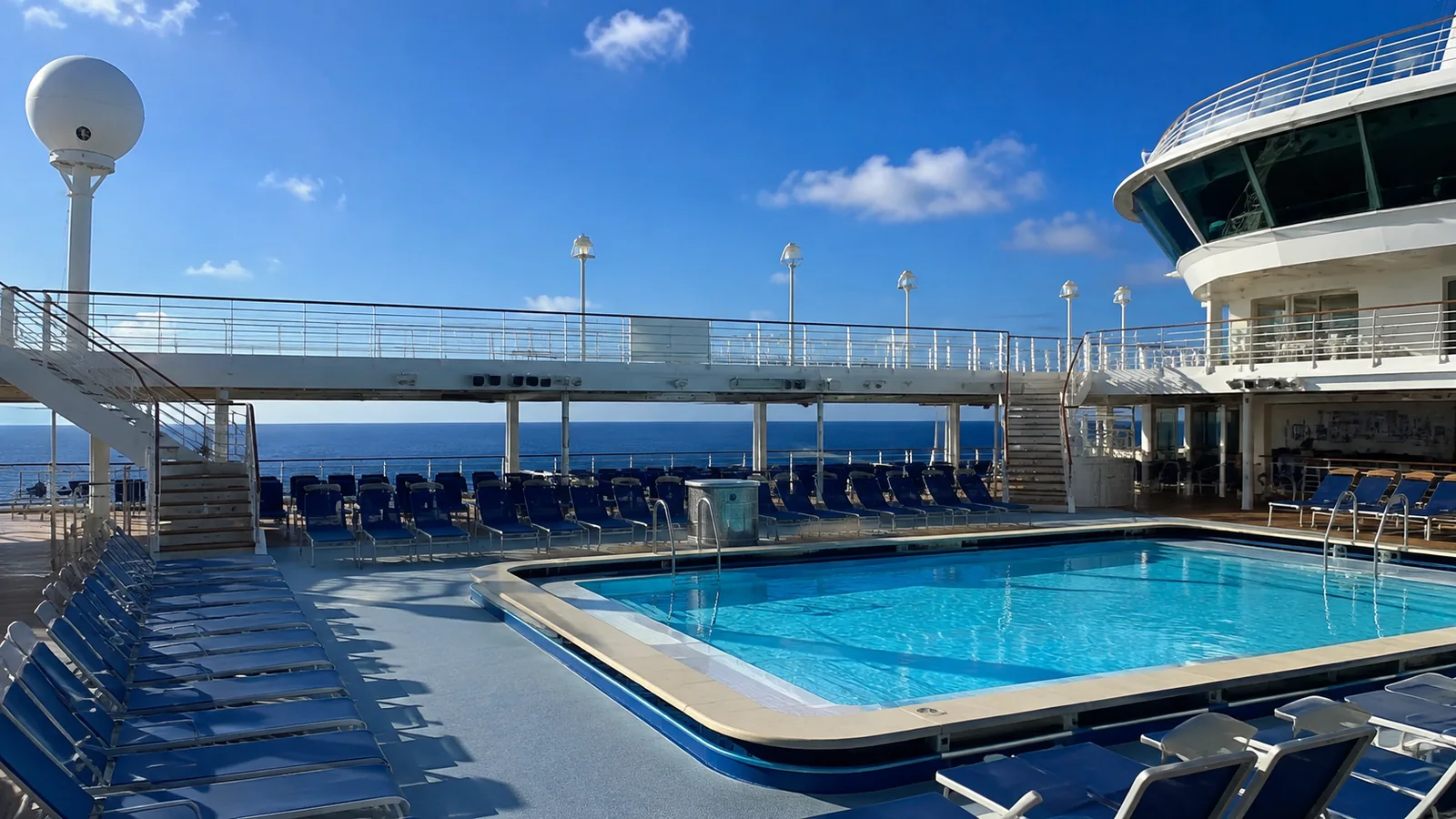 Outdoor cruise-ship swimming pool surrounded by blue loungers.