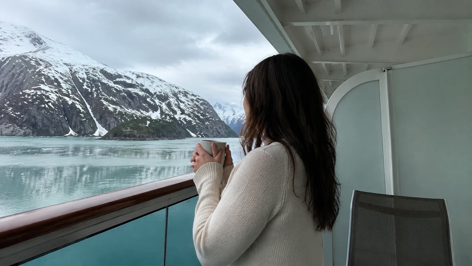 Woman holding a mug on a cruise ship deck facing a glacier