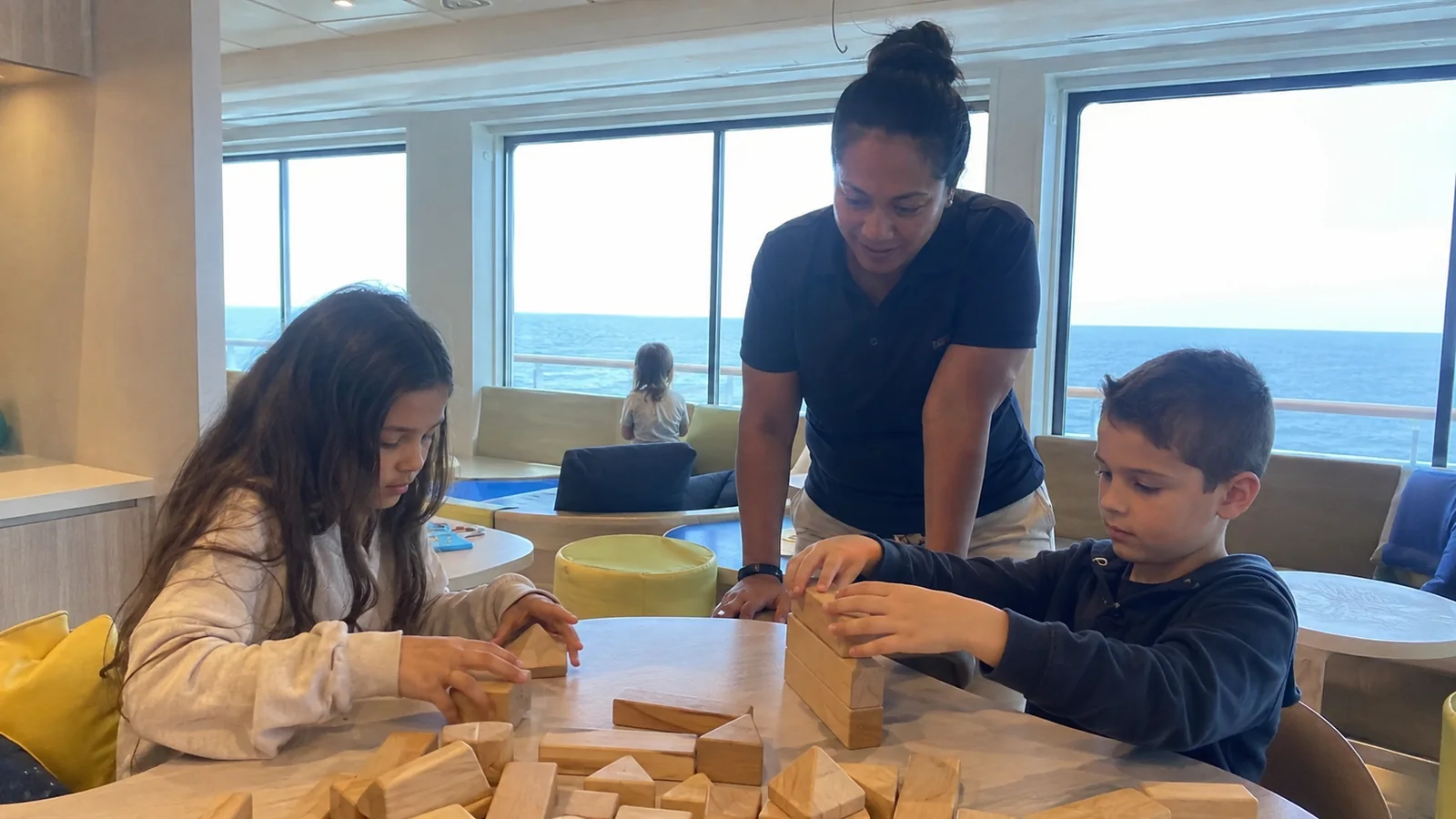 Children building with wooden blocks at a shipboard activity table with an adult supervising.
