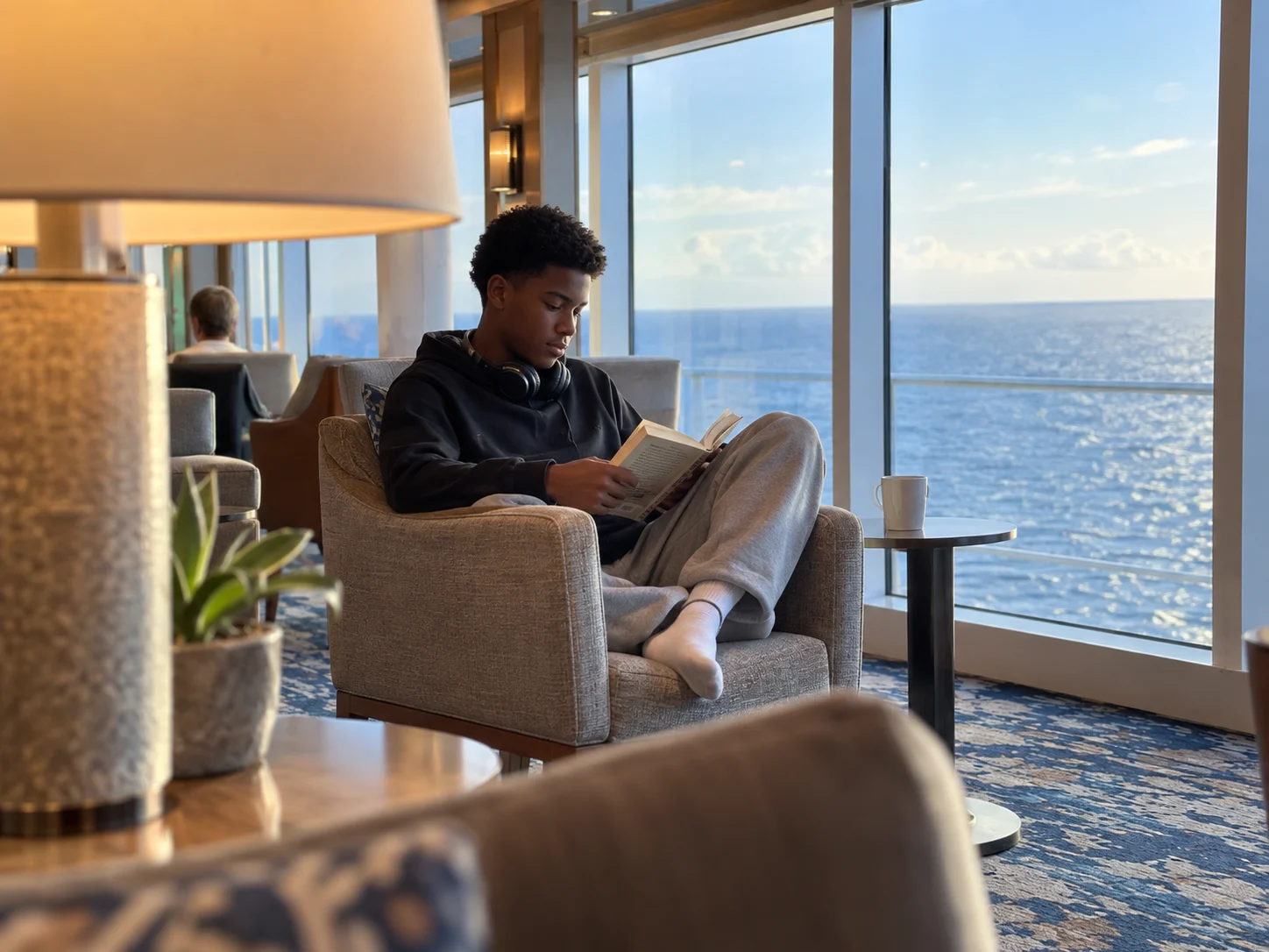 An older teenager reads quietly in an ocean-view ship lounge.