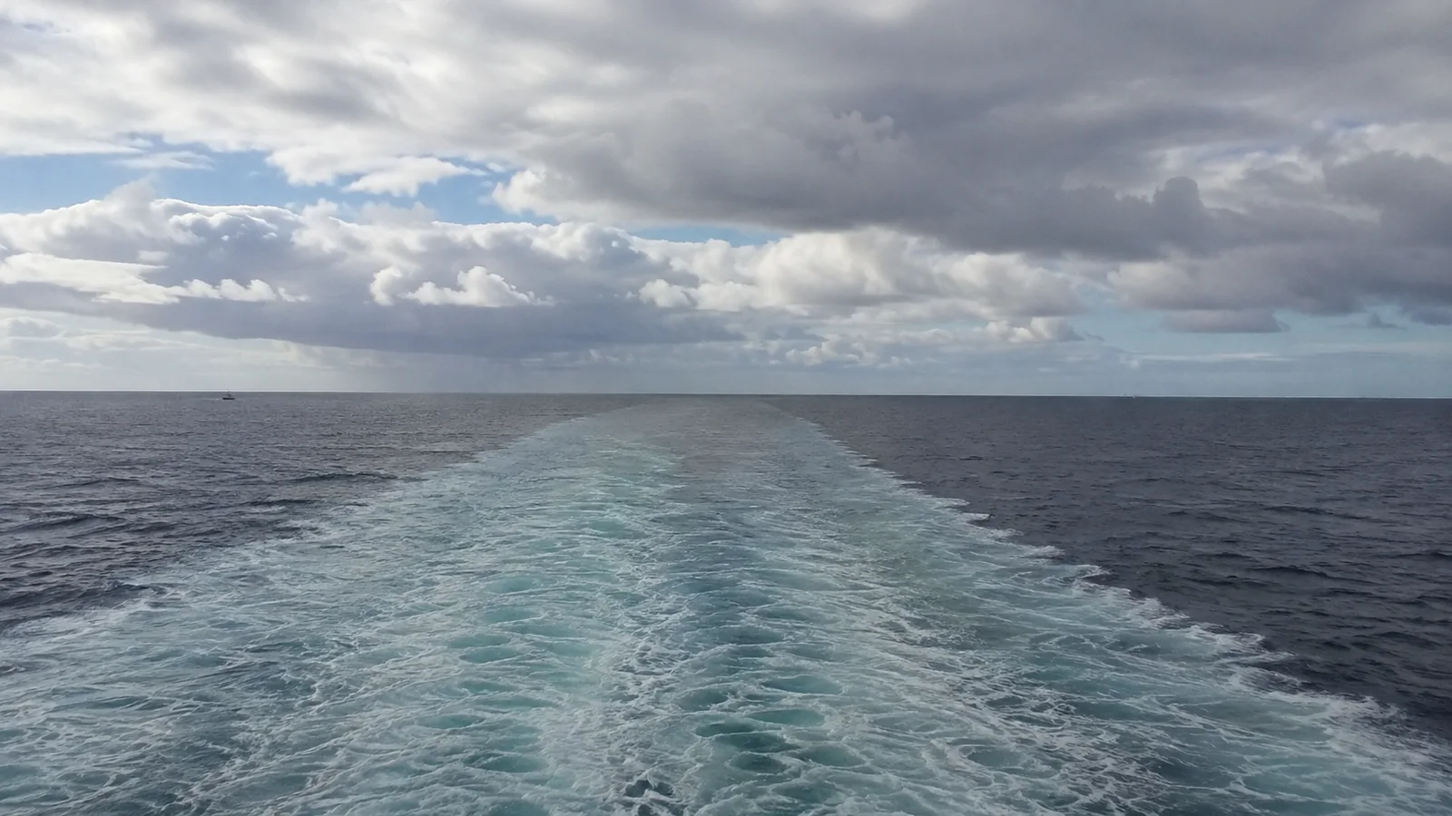 Cruise ship's wake stretching across open water under layered clouds.