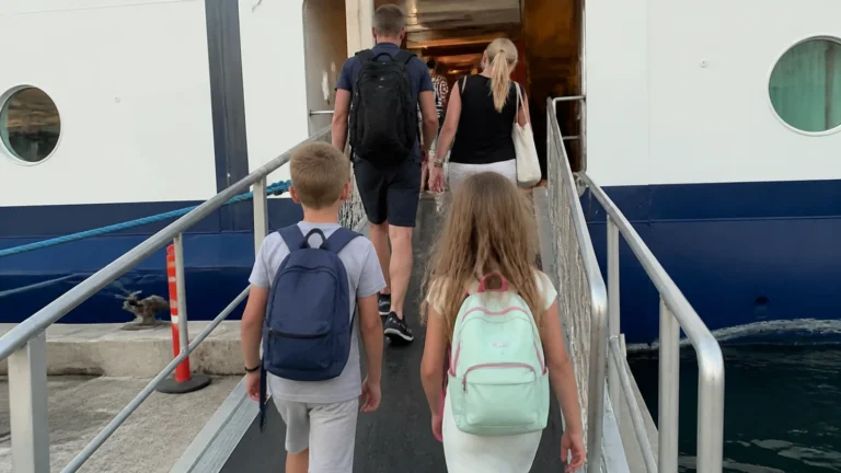 Children with backpacks following adults up a ship's boarding gangway.