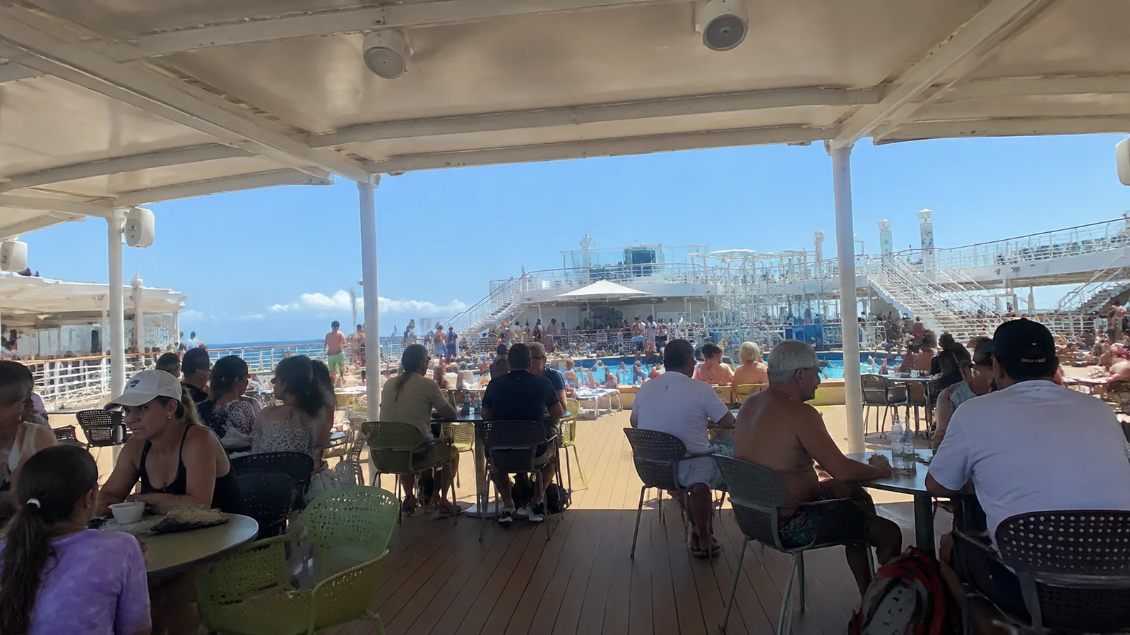 Families seated at tables on a shaded outdoor ship deck.