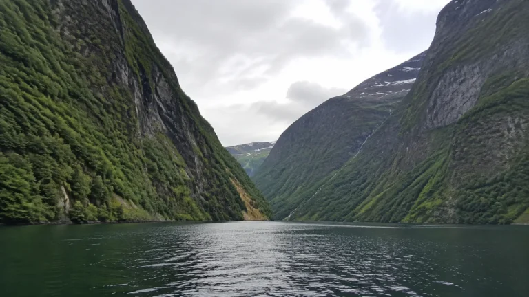 Narrow green fjord enclosed by towering steep mountain walls.