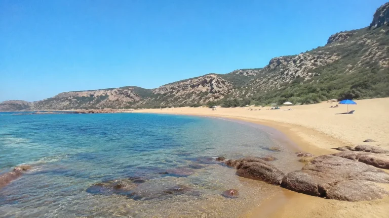 Secluded sandy cove with clear blue water and rocky hills