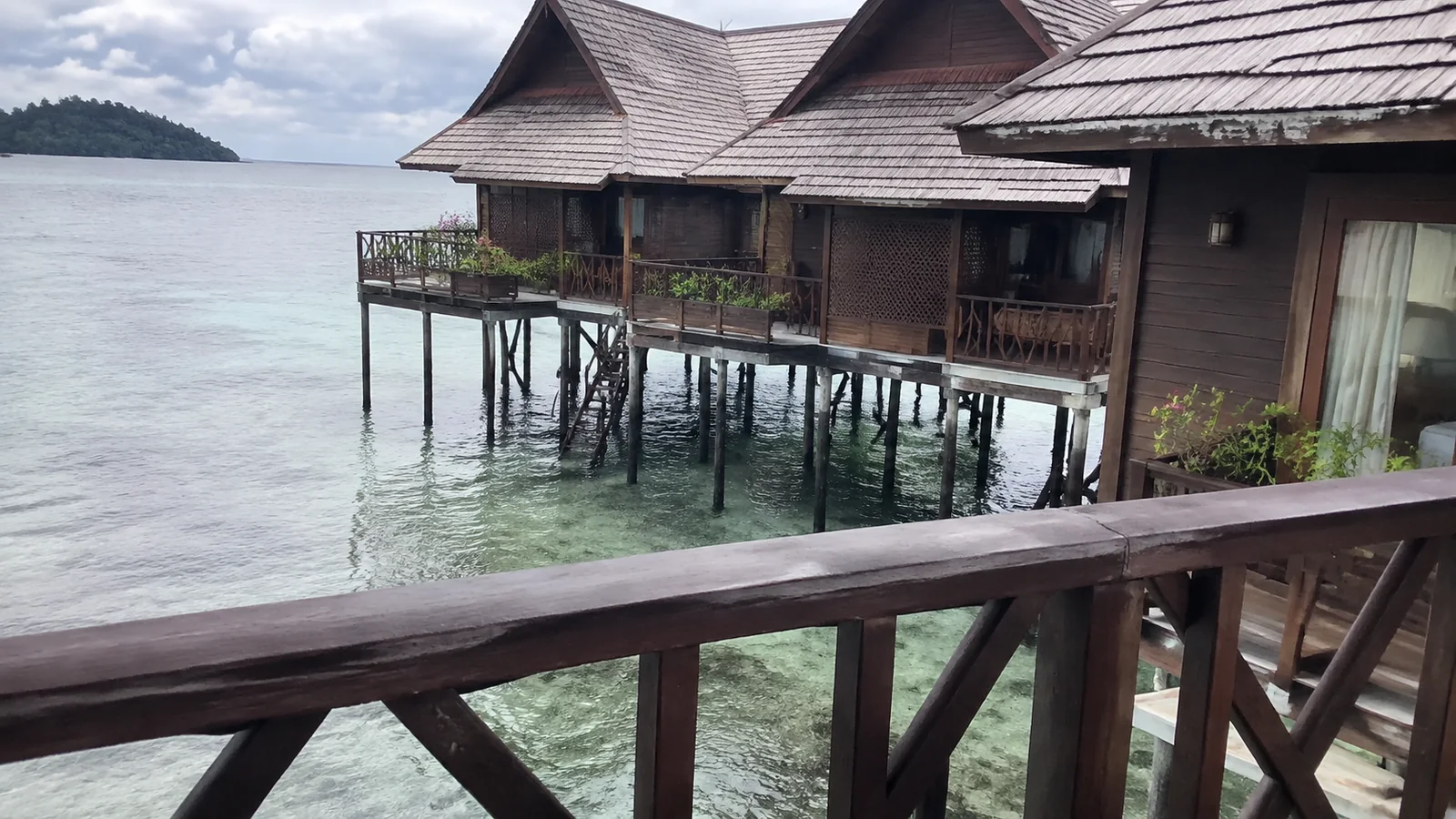 Wooden overwater chalets viewed from a shaded balcony.