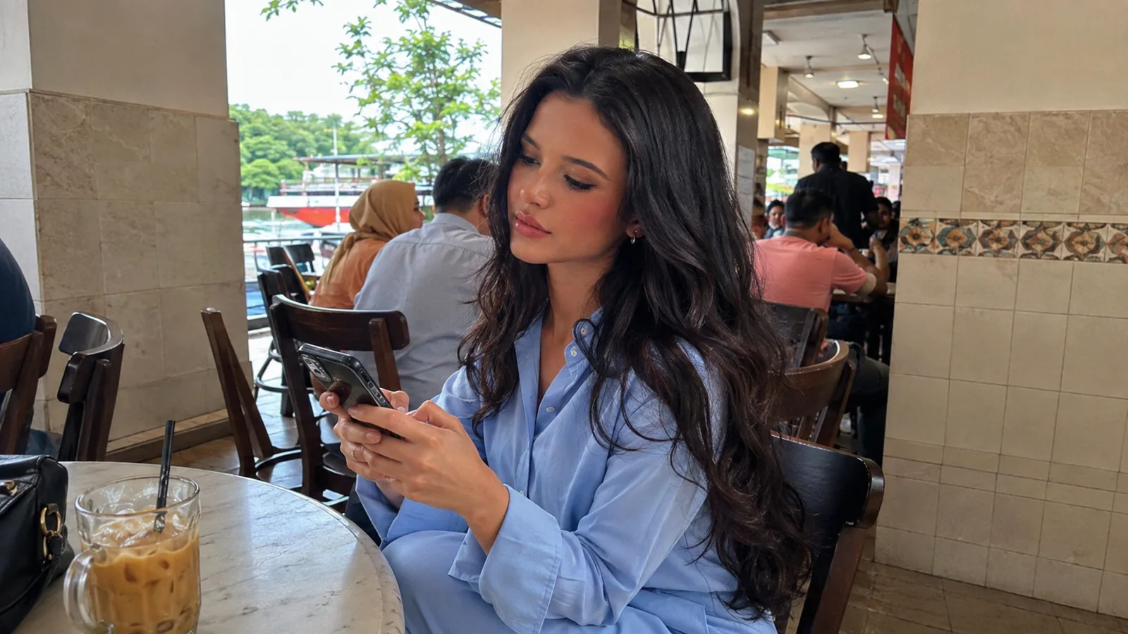 Woman checking her phone at a cafe table with an iced drink.