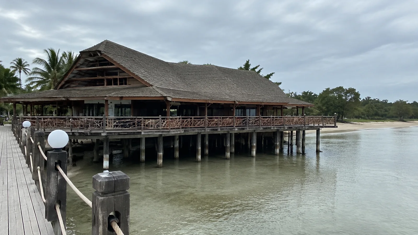 Large timber lodge on stilts beside shallow coastal water.