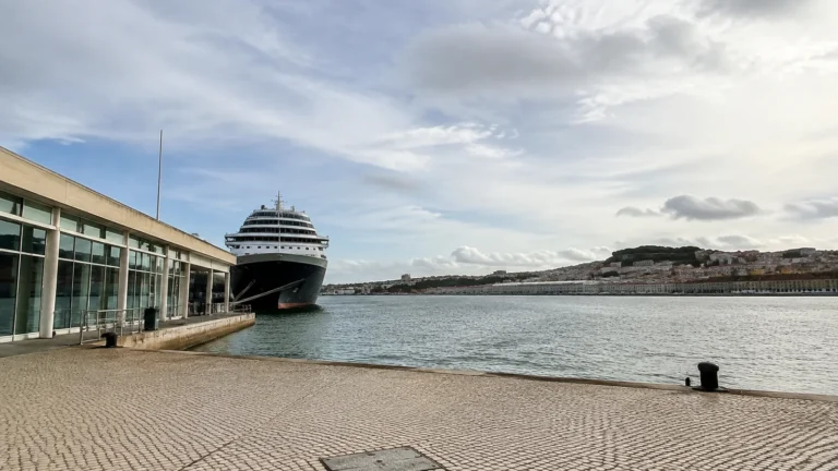 Cruise ship docked beside a long terminal building across calm water.