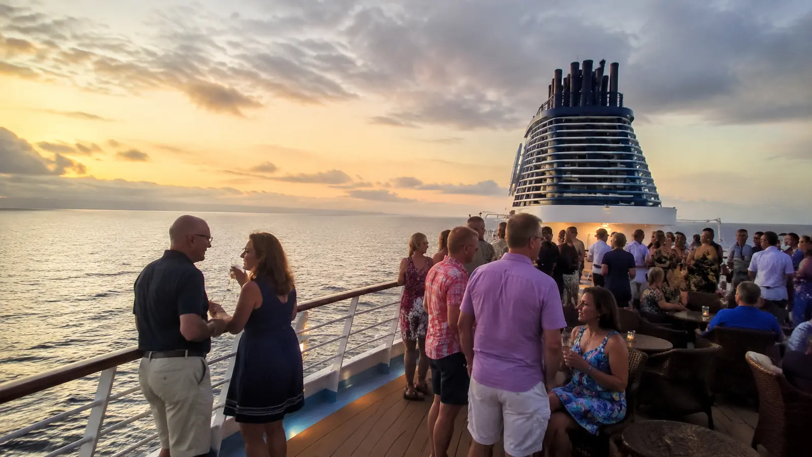 Adults socializing on an outdoor cruise ship deck at sunset