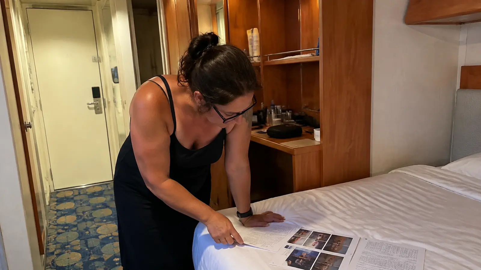 Woman leaning over a cruise cabin bed reviewing printed pages