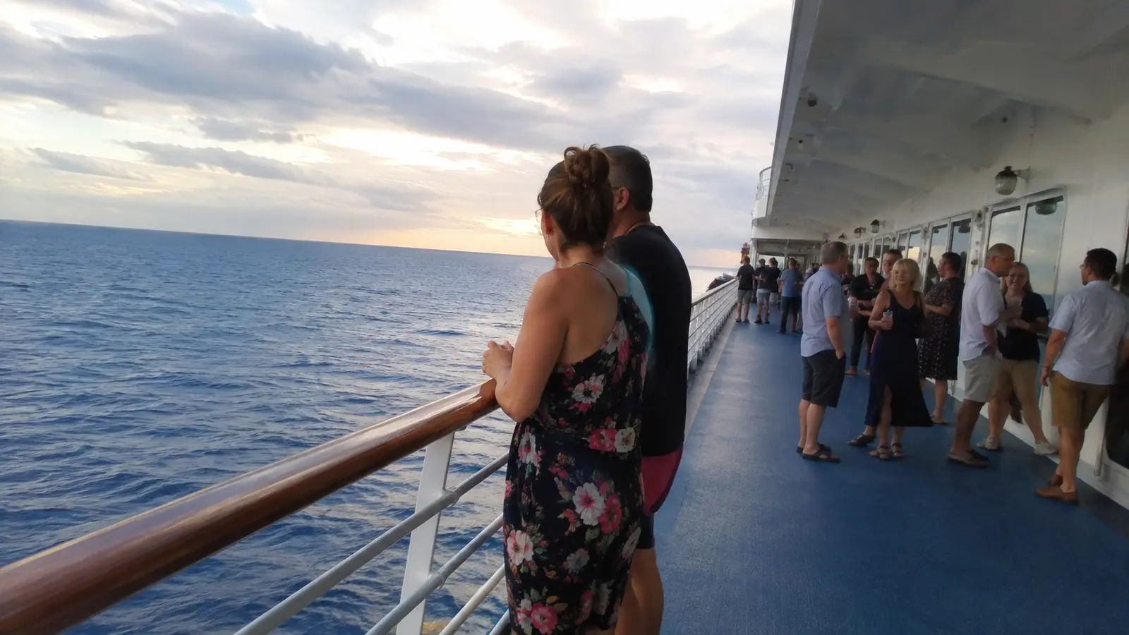 Woman standing at a cruise ship railing with other passengers nearby