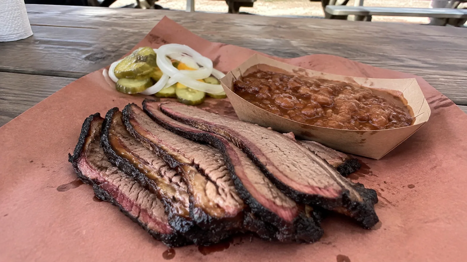 Sliced smoked meat served with beans, pickles, and onion on butcher paper.