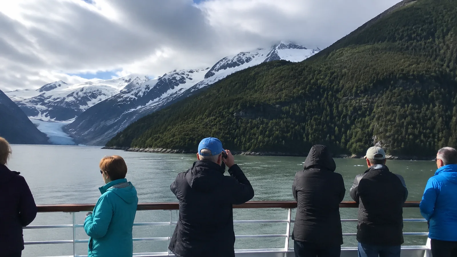 Cruise passengers photographing a glacier between snowy mountains.
