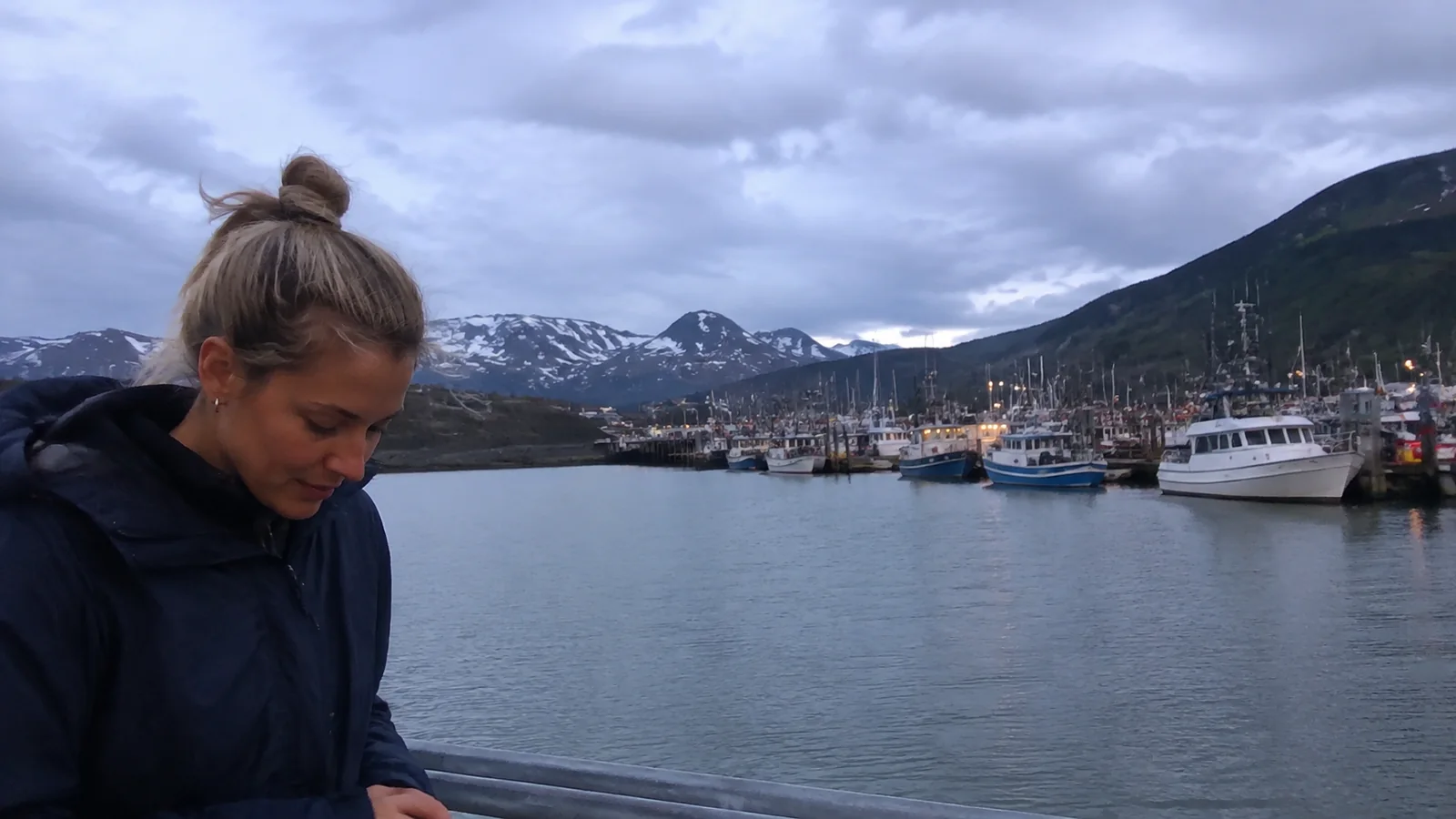 Traveler standing near a marina backed by snowy mountains.