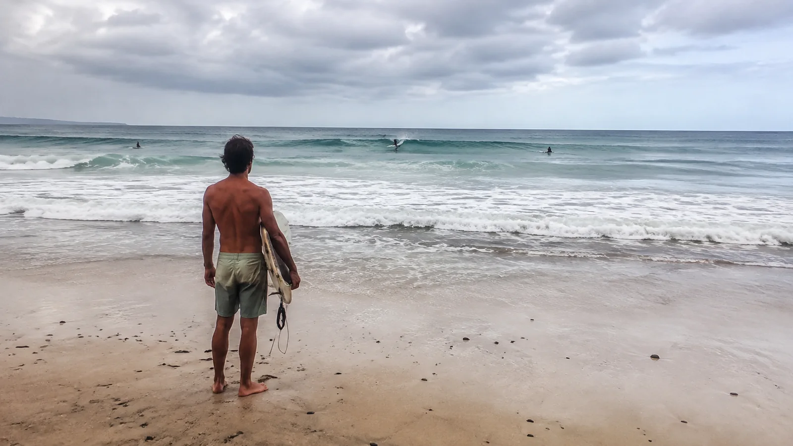 Surfer carries a board toward waves and other surfers offshore.