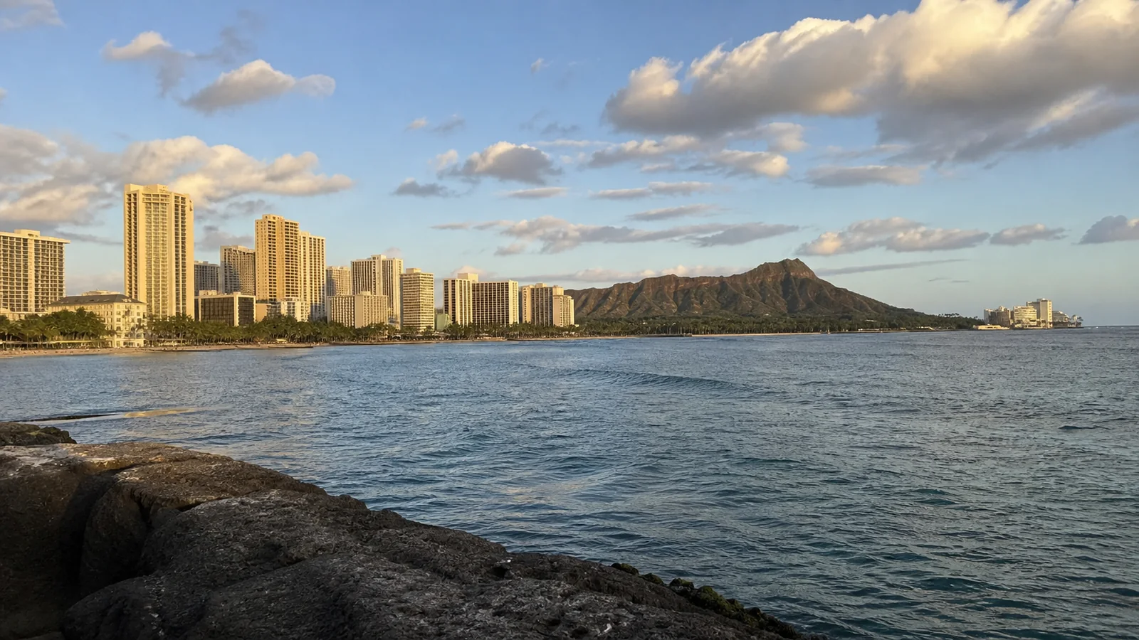 Waterfront high-rises and a volcanic ridge seen across a sunlit bay.