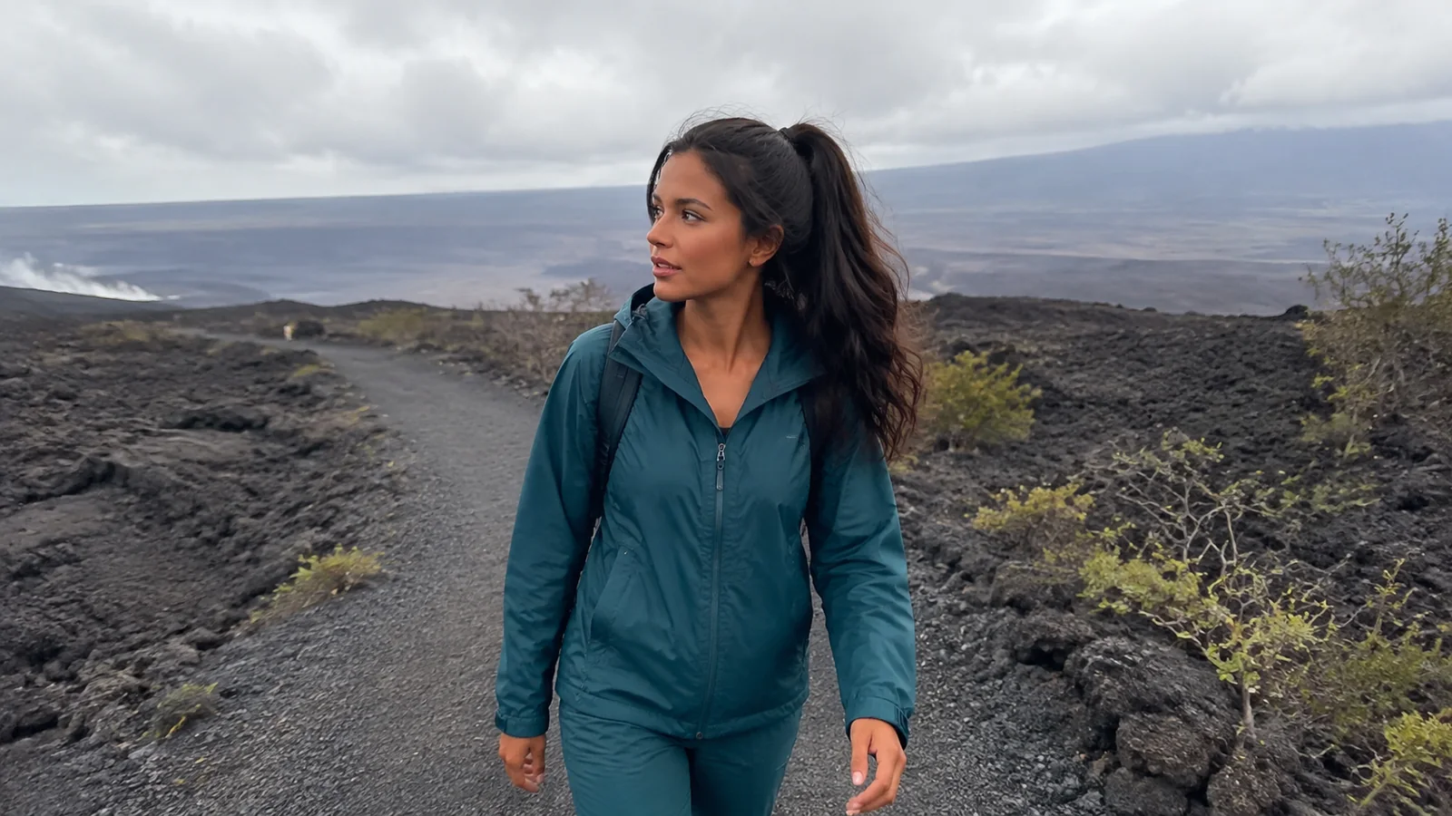Woman walks across a dark lava landscape beneath low clouds.