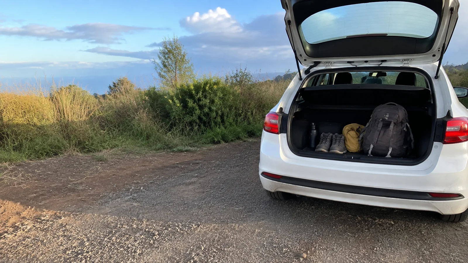 Backpack and outdoor gear sit in an open car trunk.