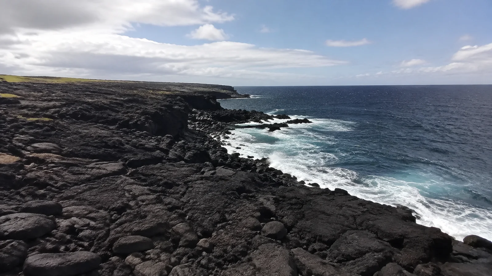 Waves break against a rugged black lava coastline.