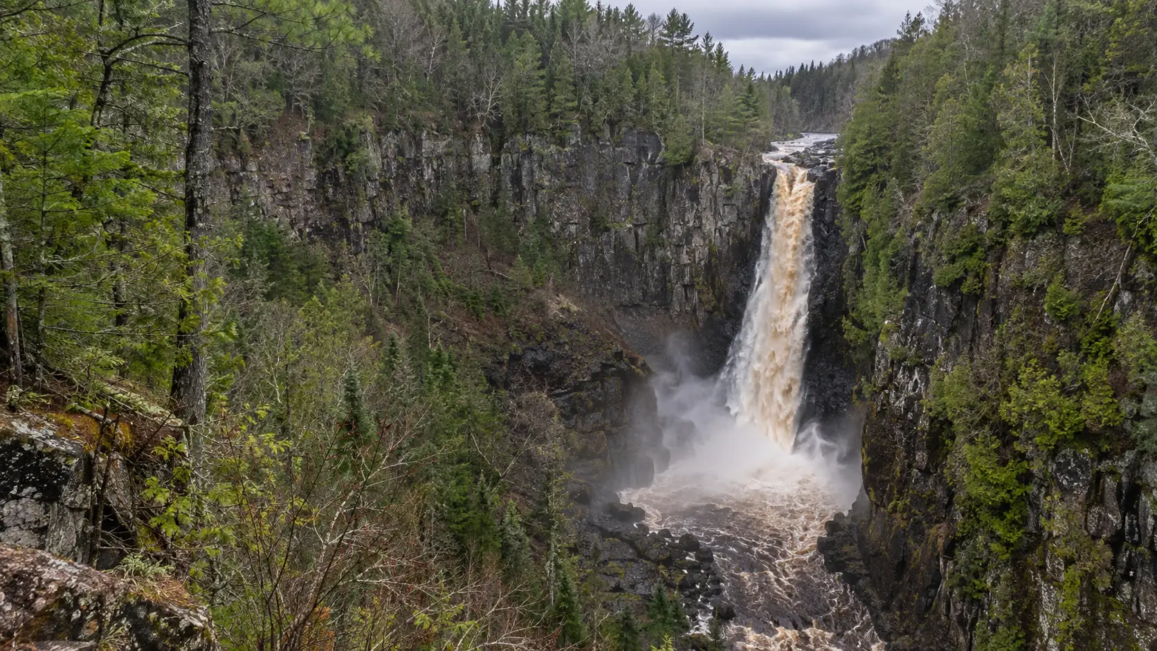 Big Manitou Falls plunging into a forested gorge at Pattison State Park in Wisconsin.